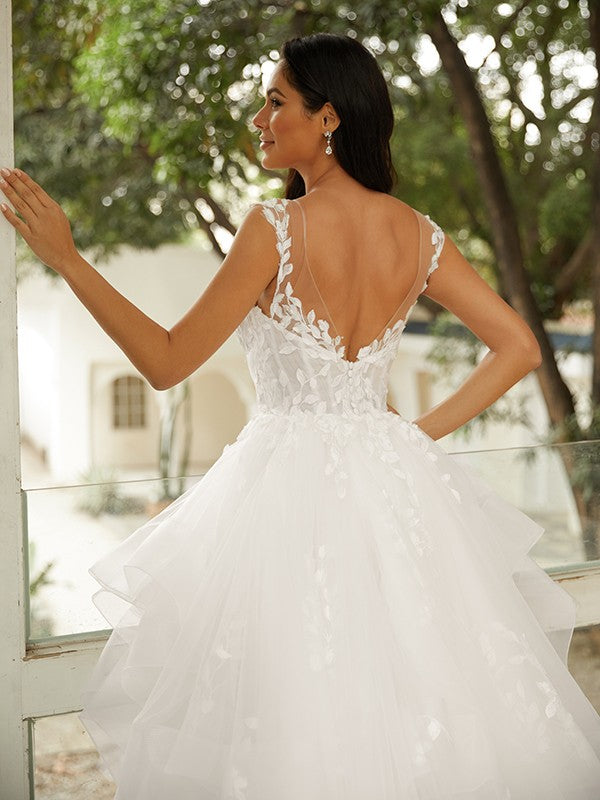 Vestido de novia de tul con apliques y escote en V, sin mangas y cola capilla.